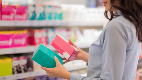 kobieta w sklepie zastanawia się, czy wybrać wkładki na nietrzymanie moczu czy podpaski menstruacyjne 