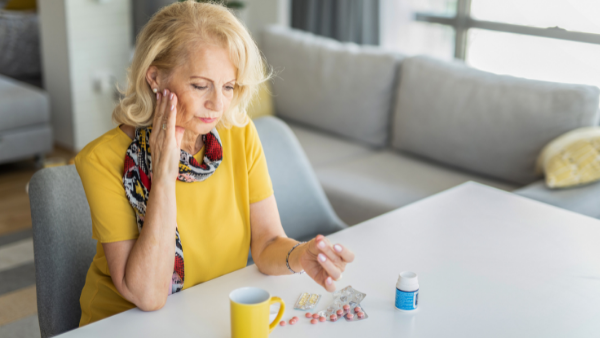 starsza kobieta siedzi przy stole i ogląda leki, które przypisuje się na nietrzymanie moczu 